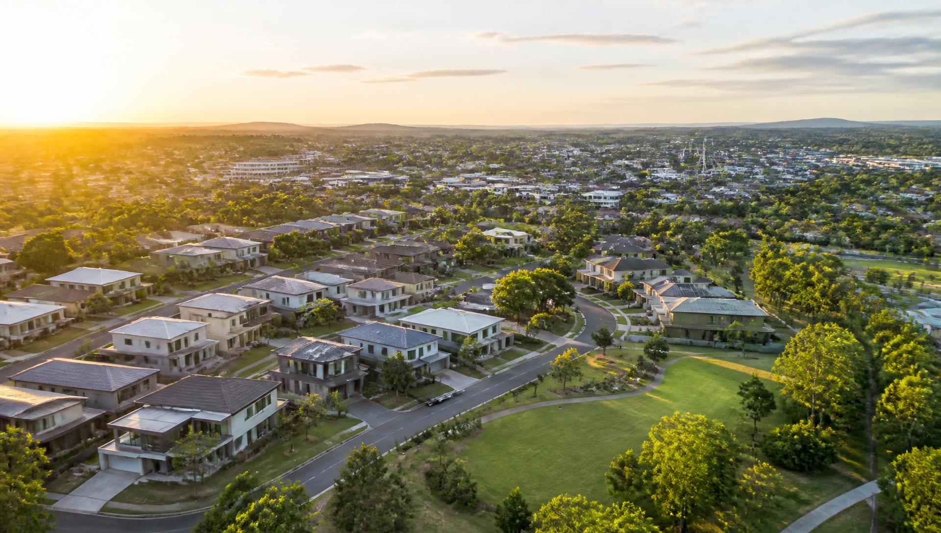 Established Australian residential street at golden hour with mature trees, footpaths and a town centre in the distance